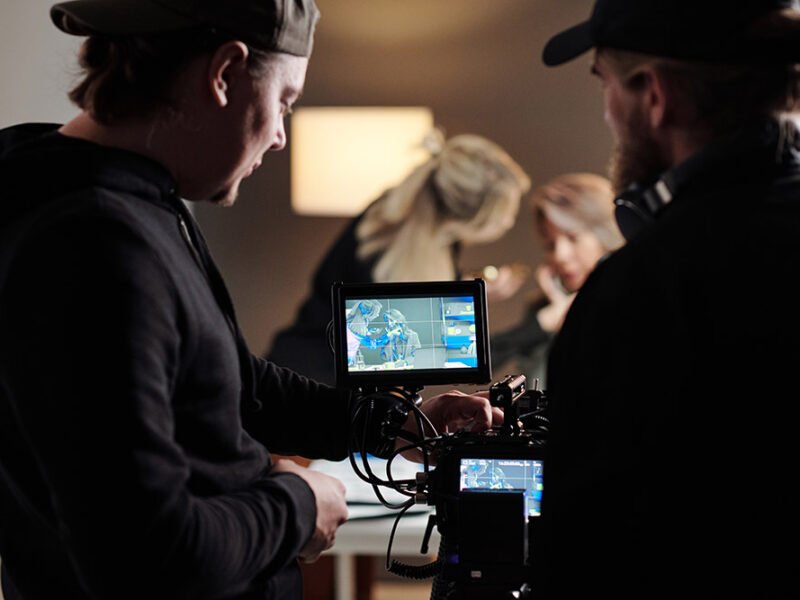 Two young men in black shirts adjusting focus of camera during shooting