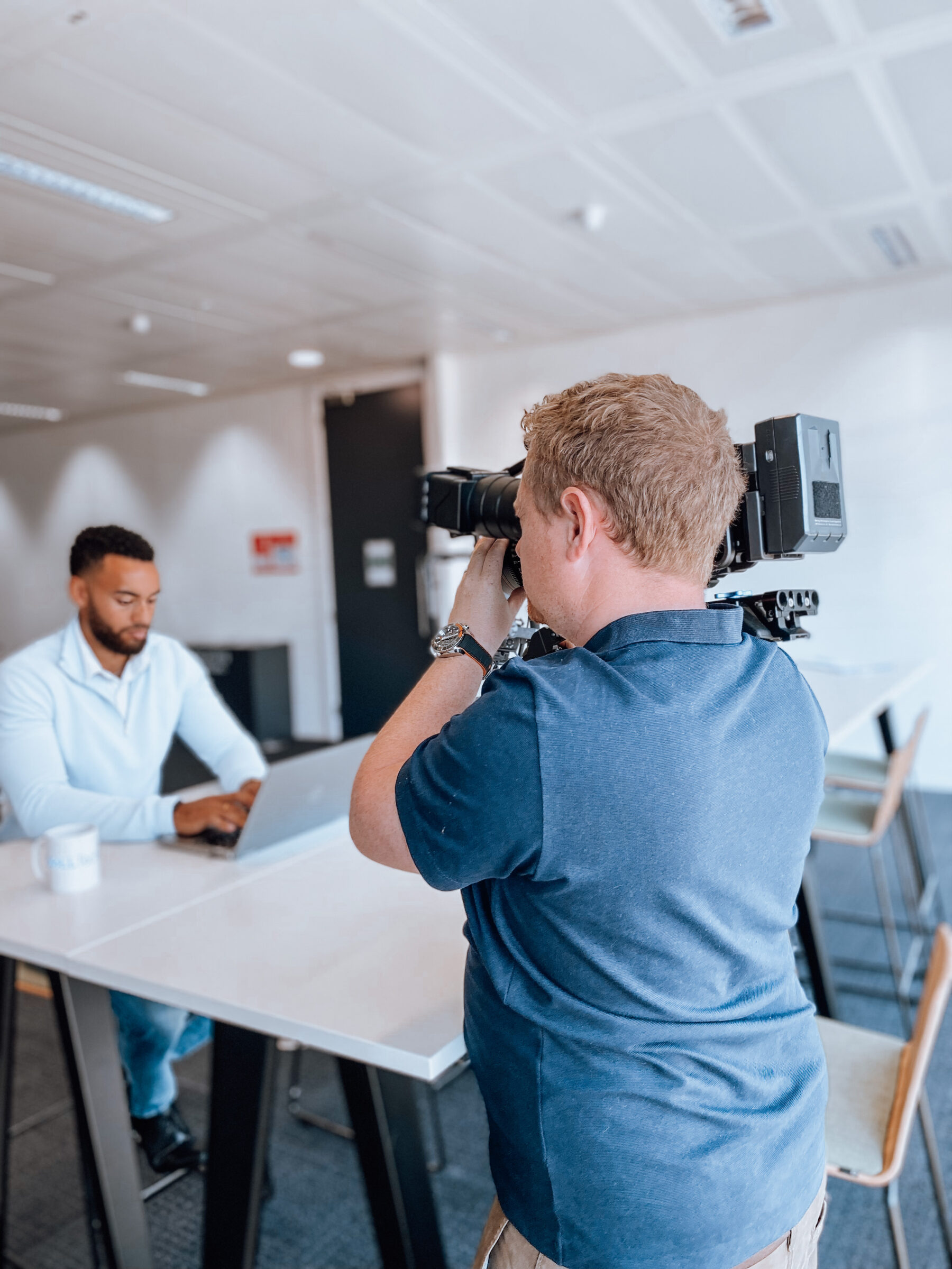 Cameraman filming a presenter working at a laptop in a modern office